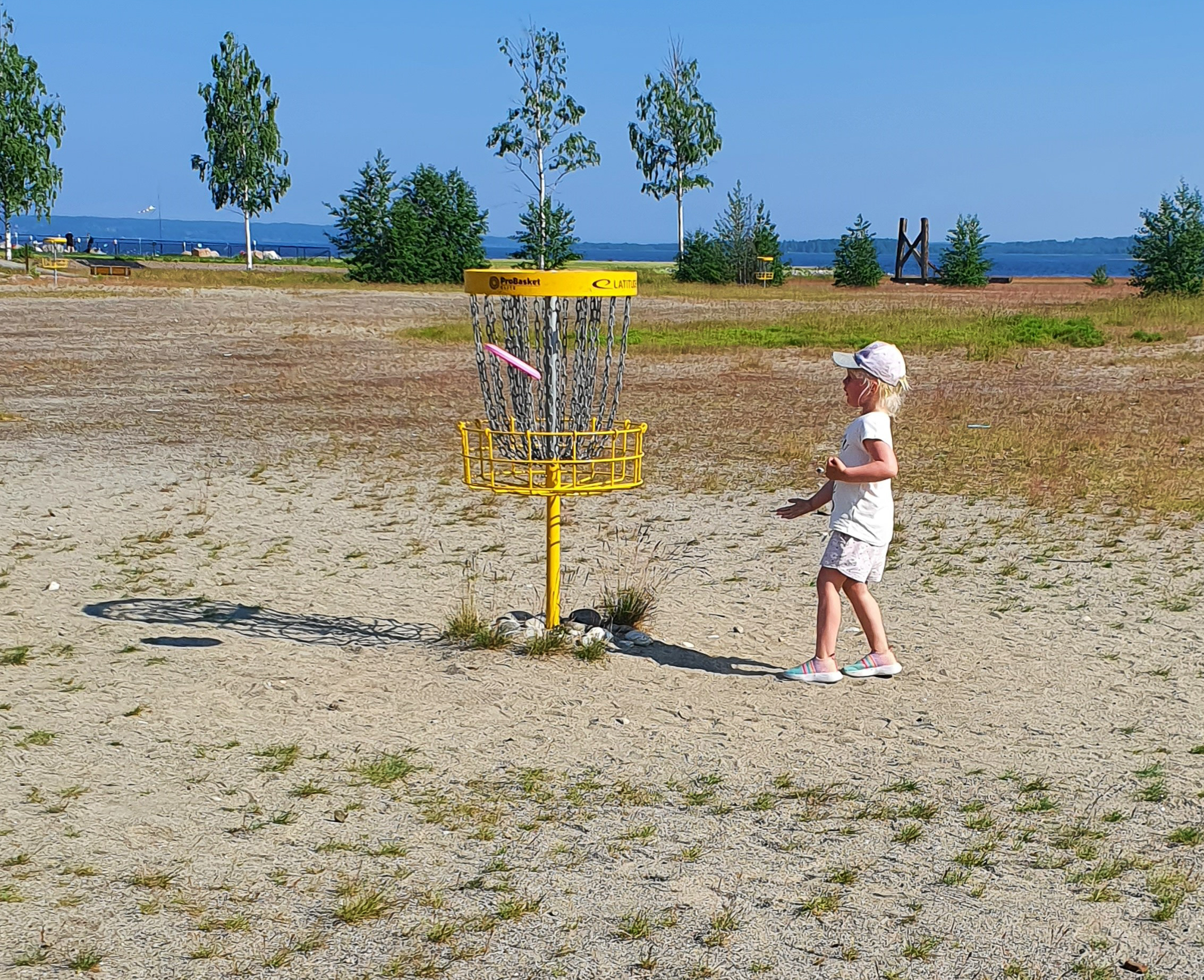 En flicka kastar iväg sin frisbee mot en gul metallkorg. Den sitter och hon har klarat av hålet.
