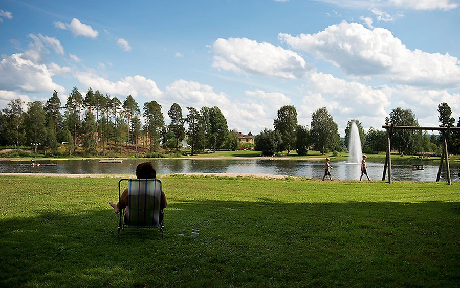 Person som sitter i solstol på en gräsmatta framför en sjö